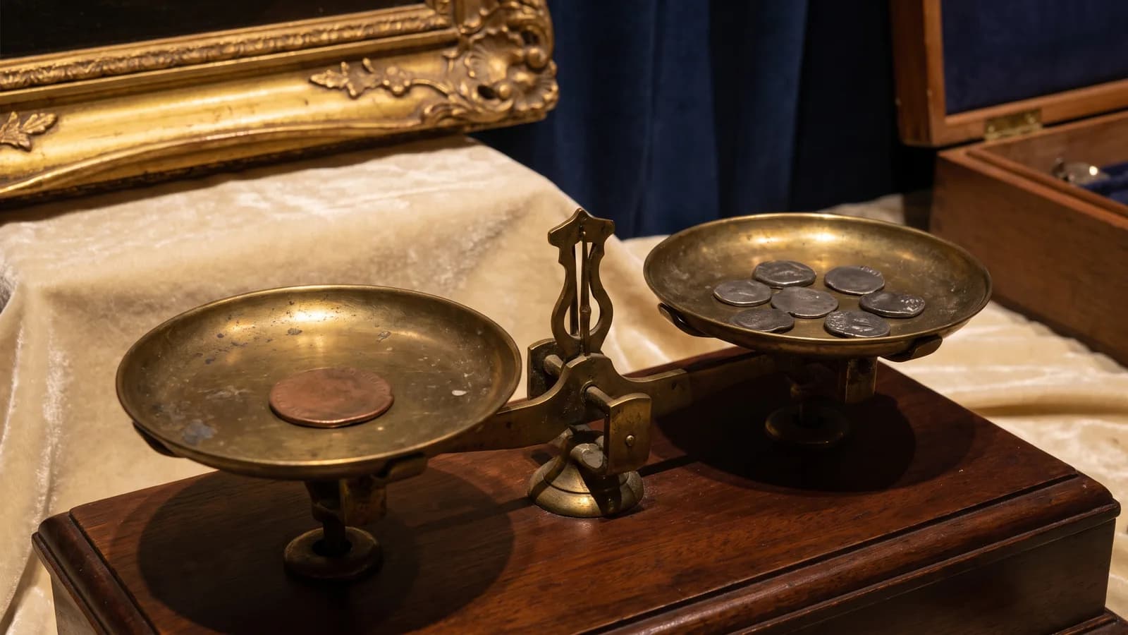 A copper token on one pan of an antique balance scale beside old coins