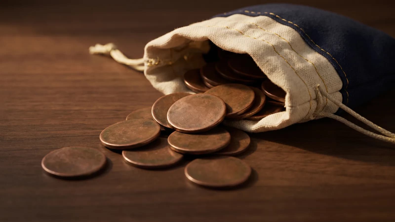 An assortment of worn copper tokens spilling from a cloth pouch onto dark wood