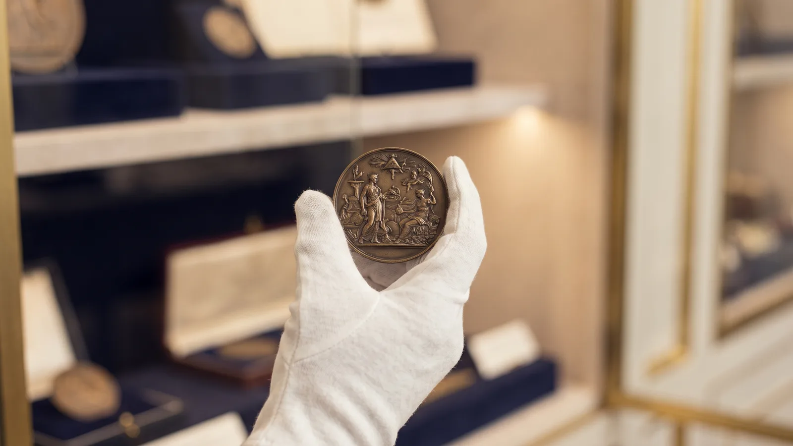 A gloved hand holding a bronze relief medal to the light