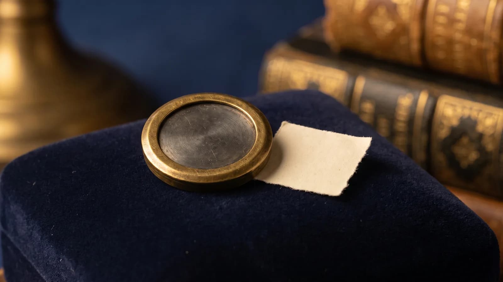 A brass-framed encased piece beside a tiny blank stamp